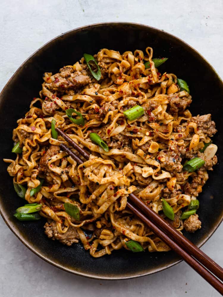 Noodles served in a black bowl. Chopsticks are shown in the picture.