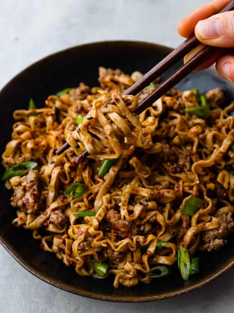 Picking up a bite of dan dan noodles with dark brown chopsticks.