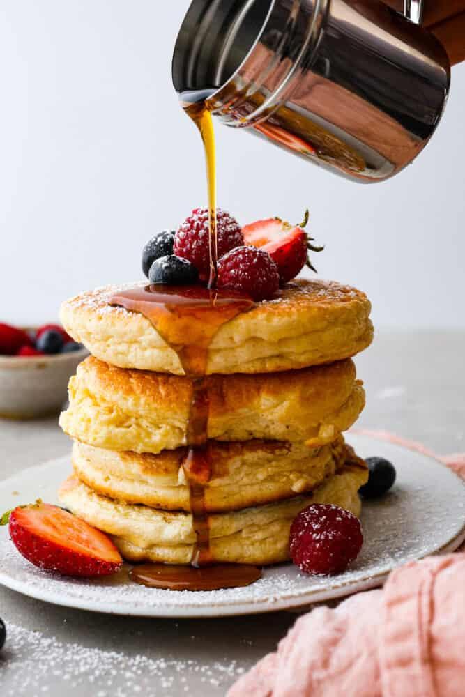 Pouring syrup over a stack of pancakes.