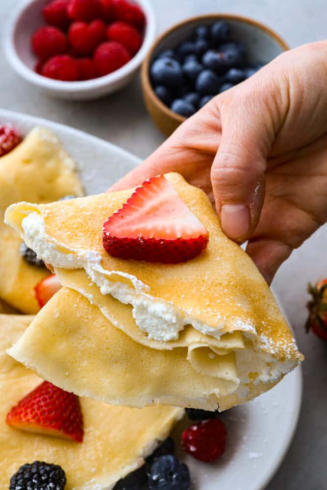 A folded crepe being held with filling on the inside and berries on top.
