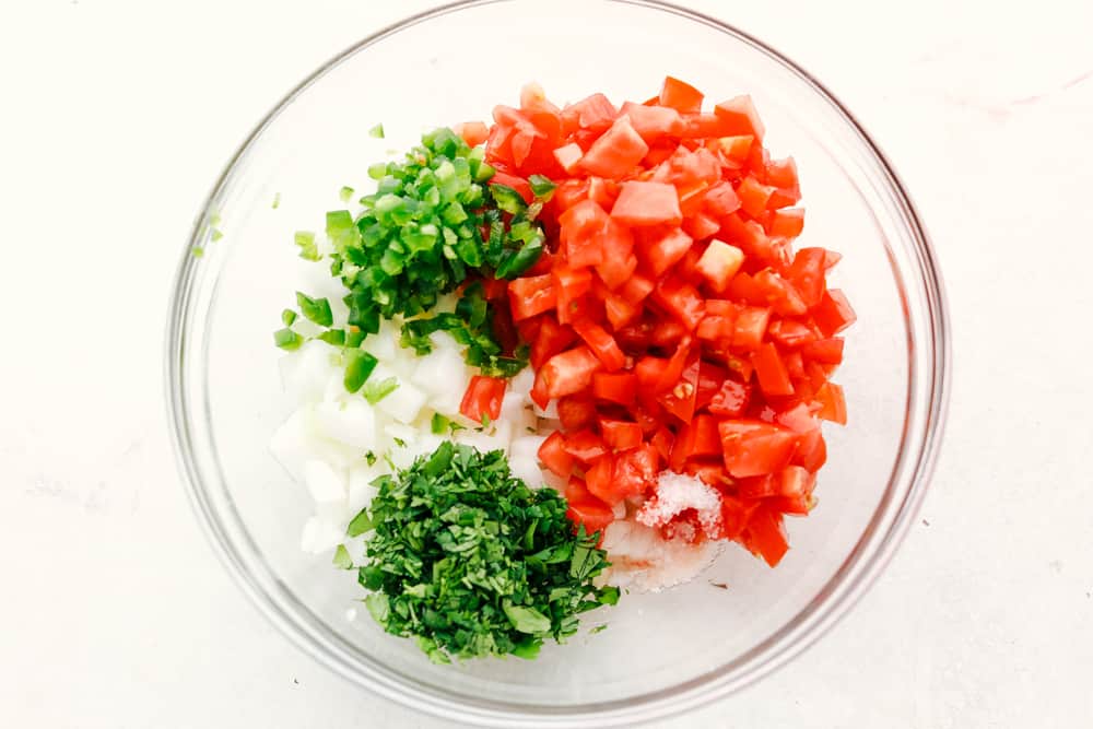 Ingredients for pico de gallo in a clear bowl.