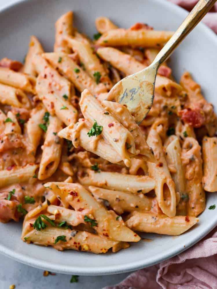 Pink sauce pasta one a plate with a gold fork taking a scoop out of the dish. 