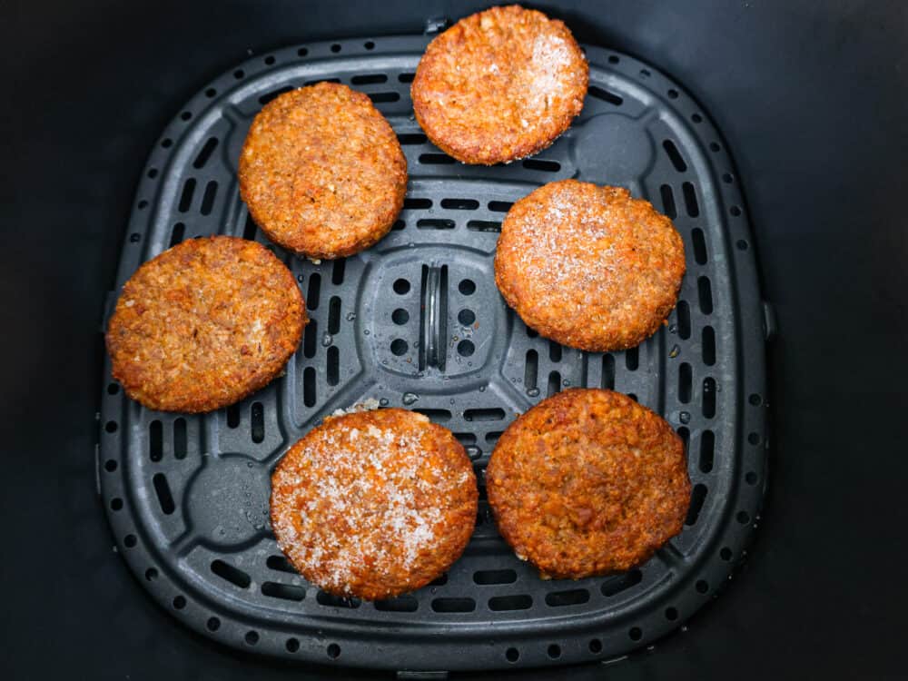 Frozen patties in an air fryer basket.