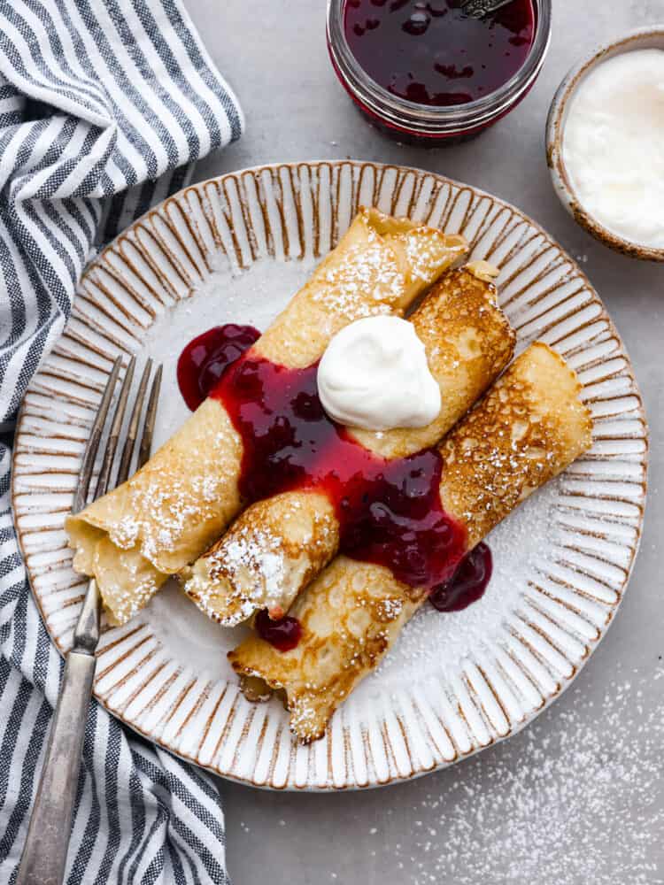 Top-down view of pancakes served with lingonberry sauce and whipped cream on a gray plate.