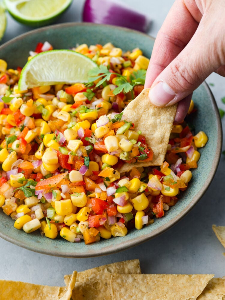 A hand dipping a tortilla chip into the corn salsa. 