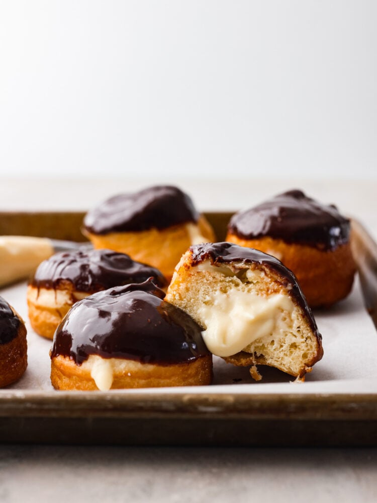 The side view of a Boston cream donut cut open with the filling coming out. 