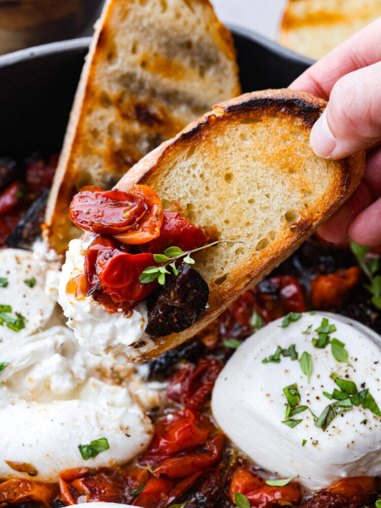 Scooping up tomatoes and cheese with a piece of toasted, sliced baguette.