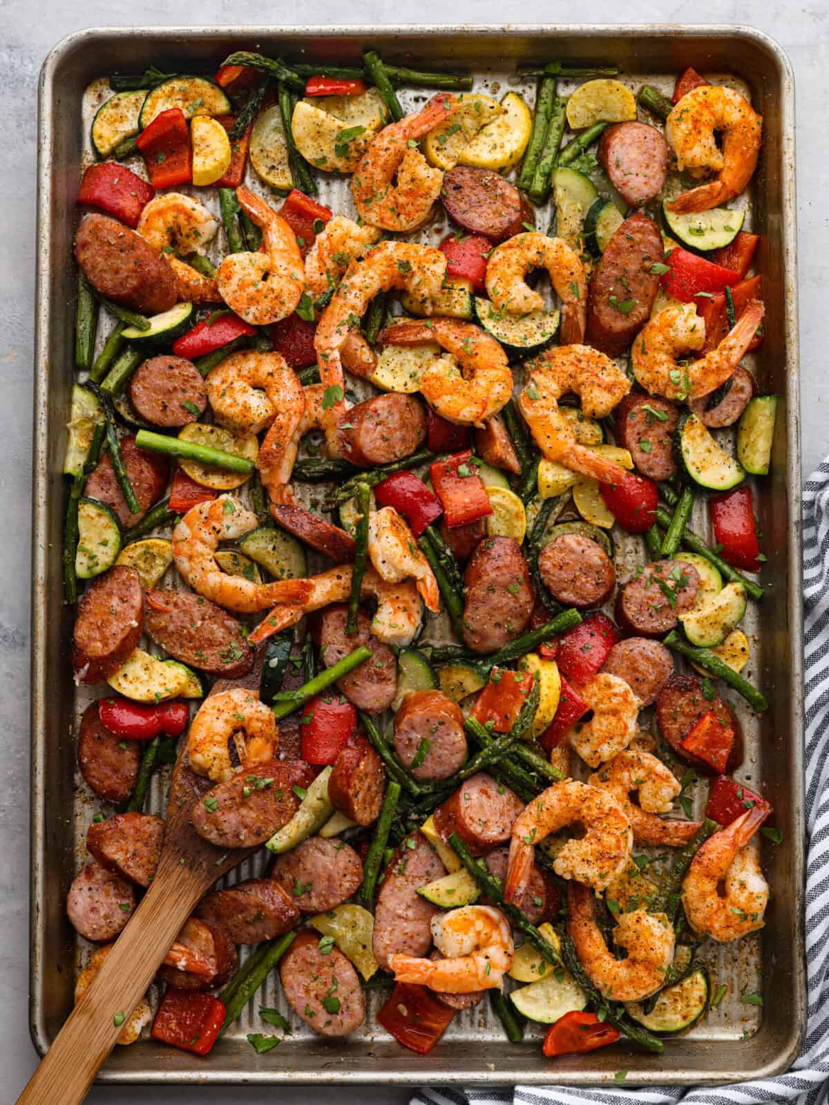 Top view of cajun shrimp and sausage sheet pan on a sheet pan. A striped towel is next to the sheet pan.