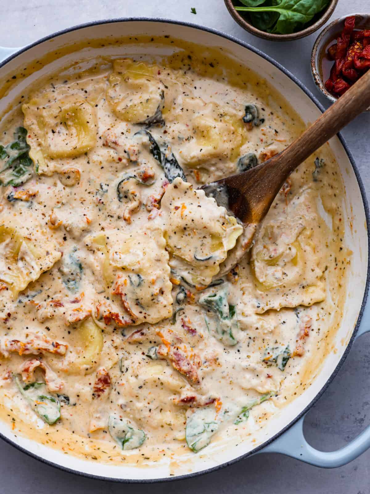 Top-down view of creamy Tuscan ravioli in a blue and white skillet.