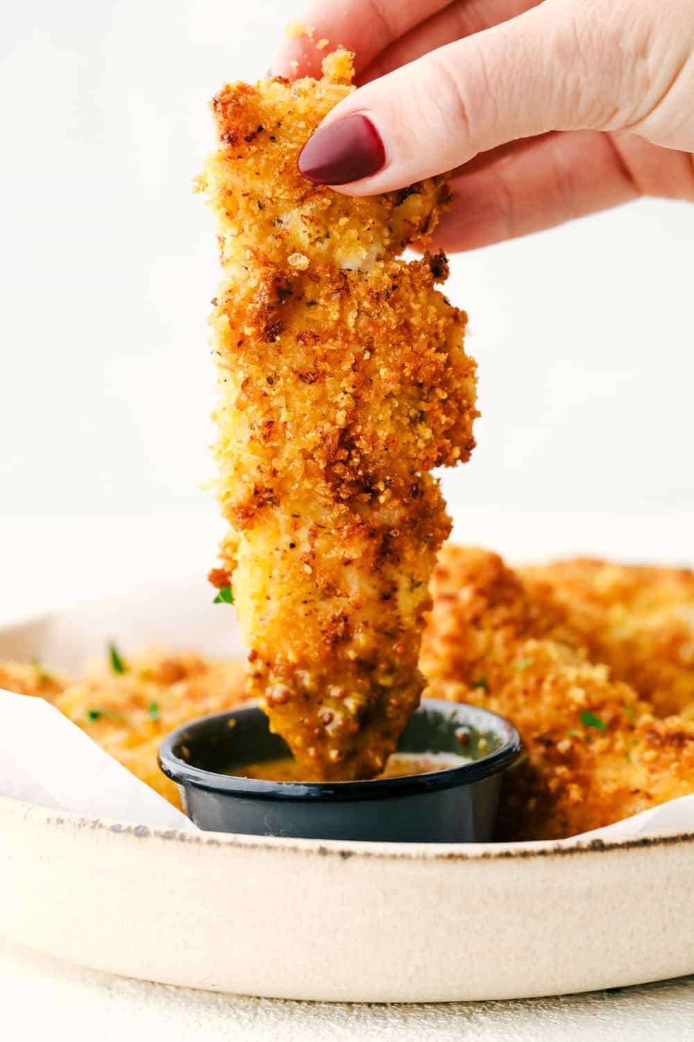 Crispy golden Air Fryer Chicken Tenders being dipped in honey mustard sauce.