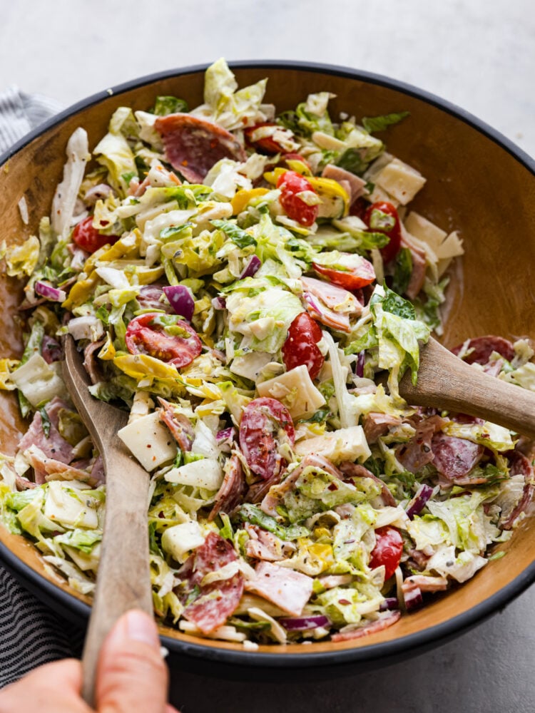 Grinder salad being tossed with 2 wooden spoons.