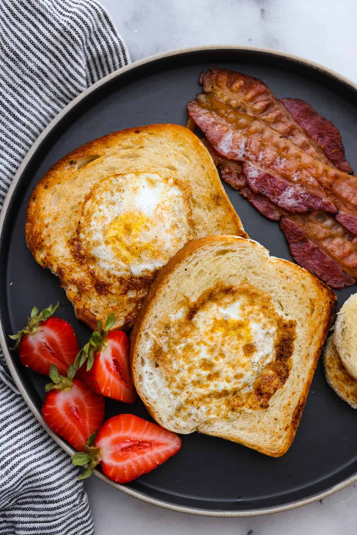 2 slices of egg in a hole served with bacon and strawberries.