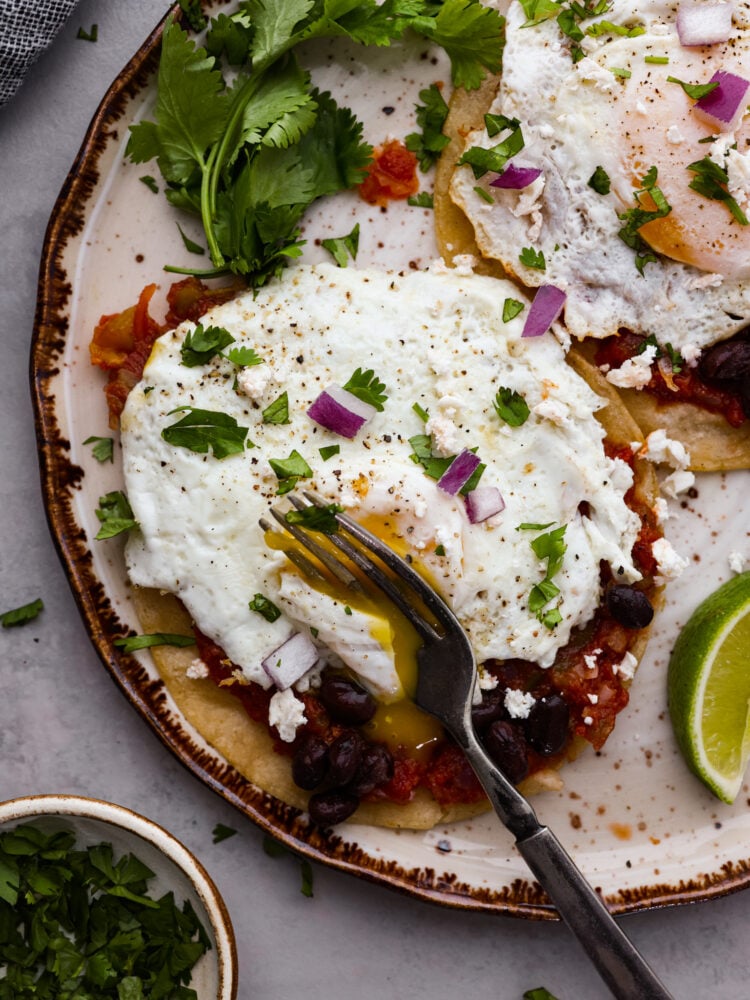 Close overhead view of a fork cutting into the fried egg of huevos rancheros.