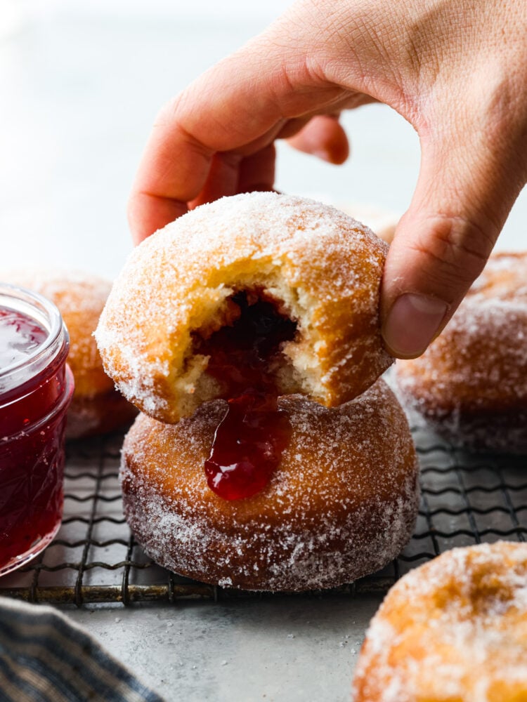 Picking up a jelly donut. A bite has been taken out of it, so the strawberry filing is exposed.