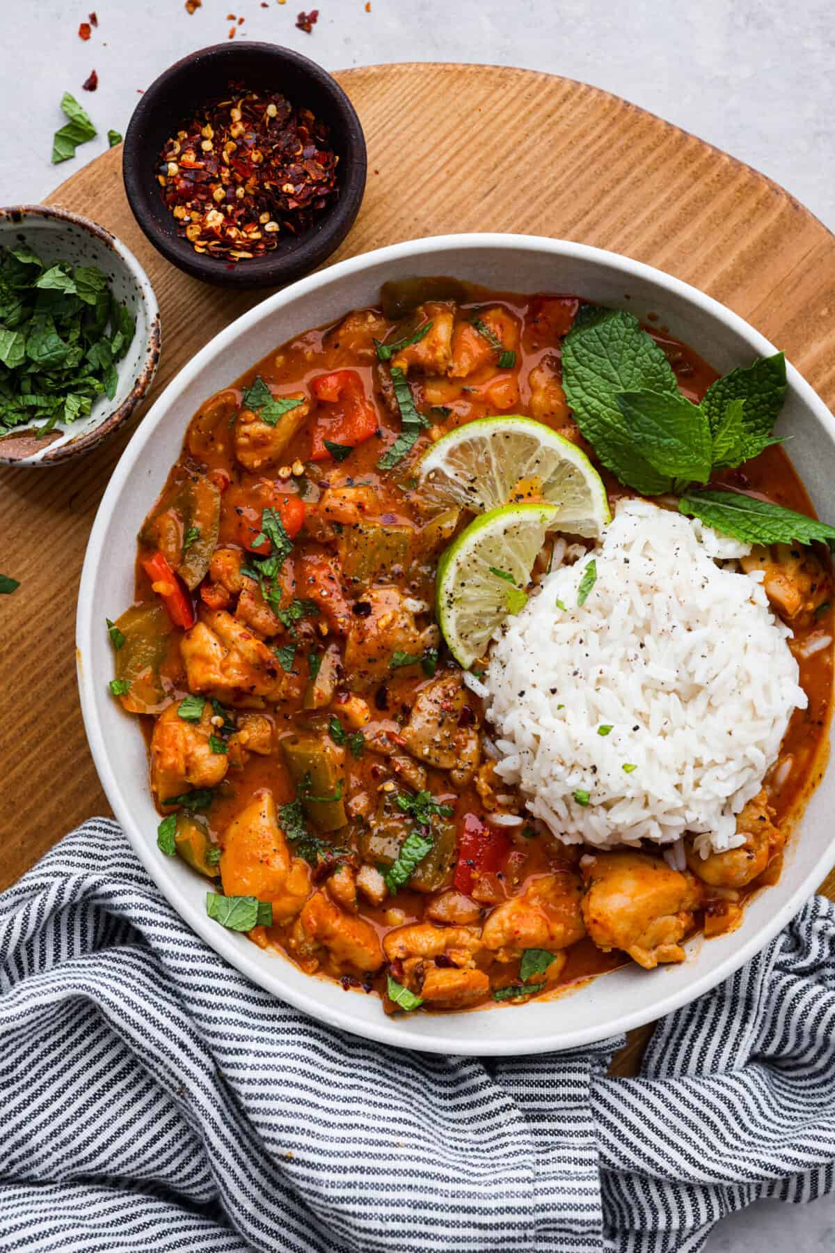 Panang curry in a bowl on a wooden cutting board with two bowls os spices on the side. 