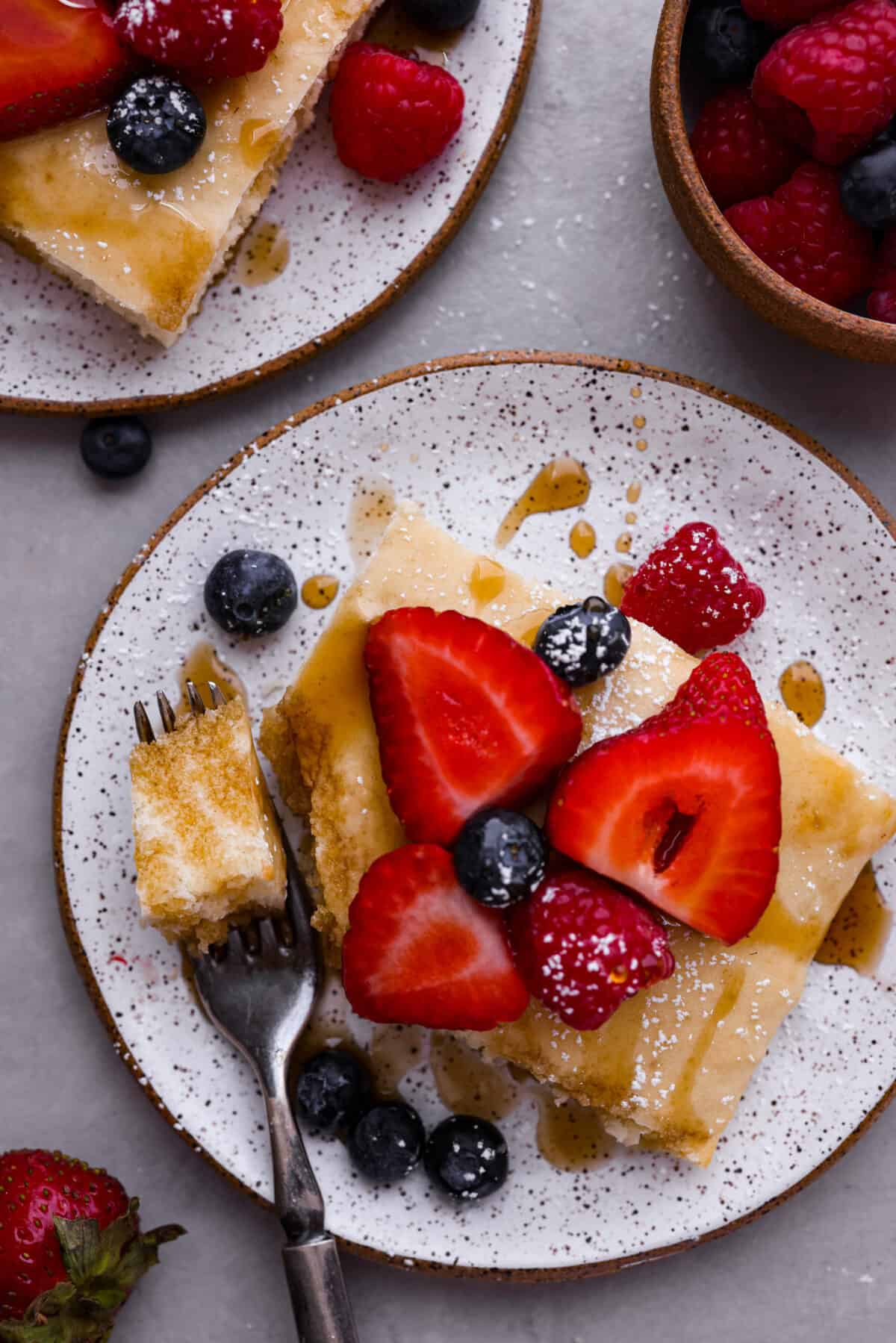 Top-down view of sheet pan pancakes topped with powdered sugar, syrup, and berries.