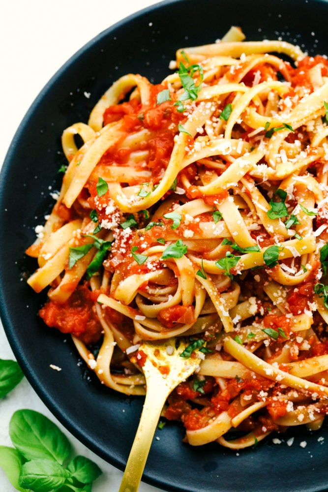 Marinara sauce mixed in with thick linguine pasta in a bowl with a fork stuck in it. 