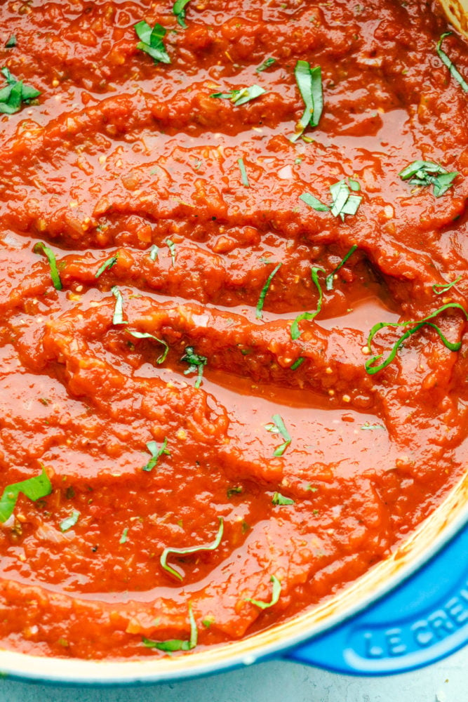 Marinara sauce in a stove top pan garnished with herbs.