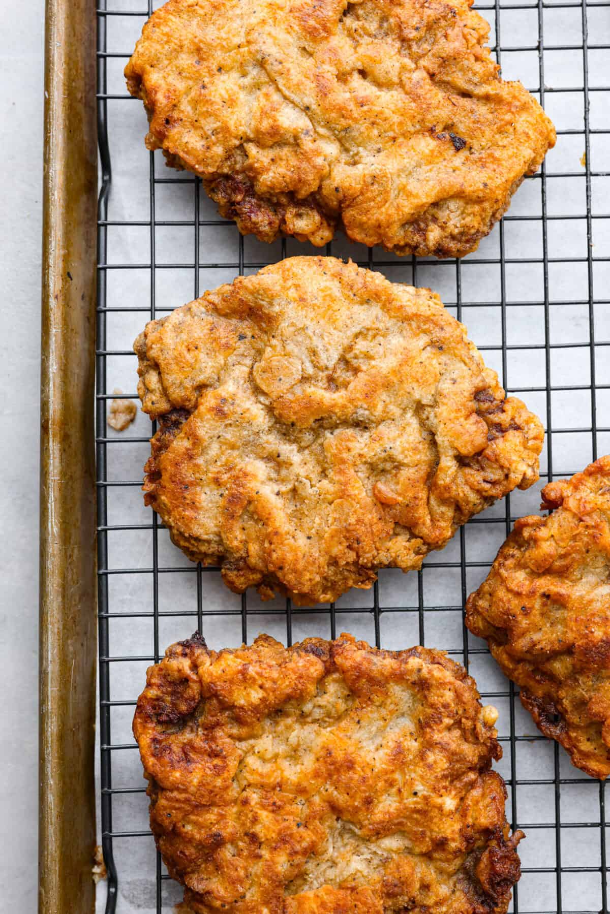 Top-down view of chicken fried steaks on a wire rack.