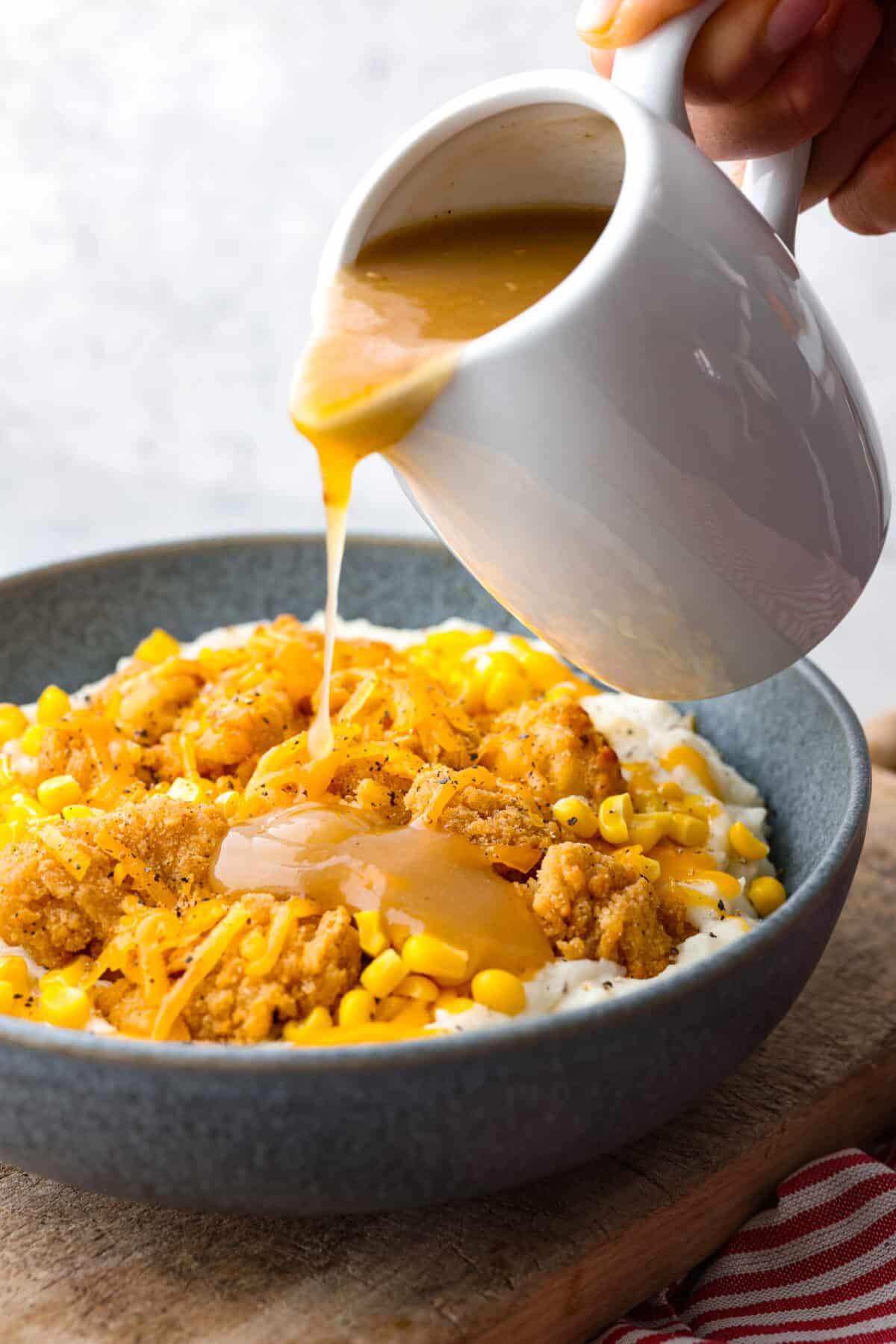 Pouring gravy over chicken, corn, and mashed potatoes.