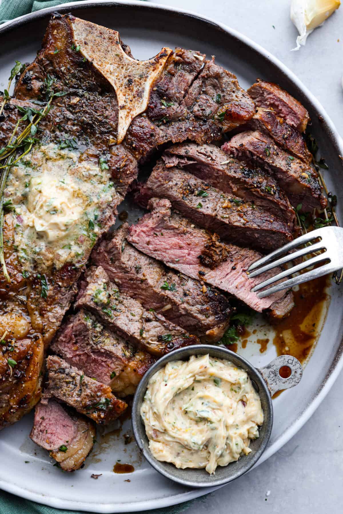 The meat is cut into slices and served on a gray plate with compound butter.