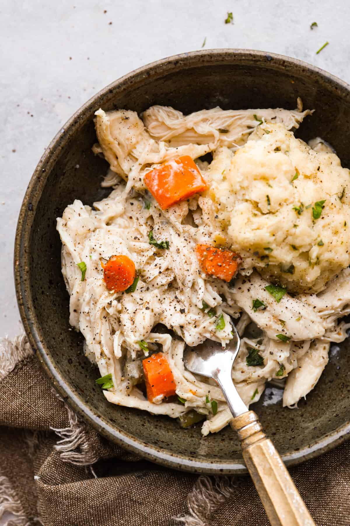 Chicken and dumplings in a brown bowl with a fork.