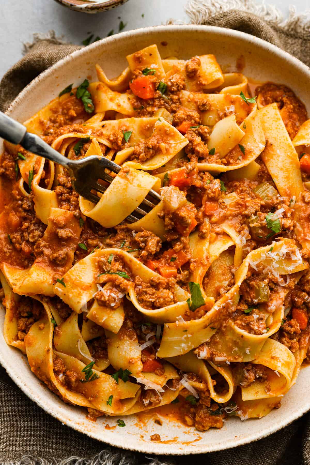 A closeup of slow cooker ragu with pasta in a bowl with a fork that has some pasta swirled around it. 