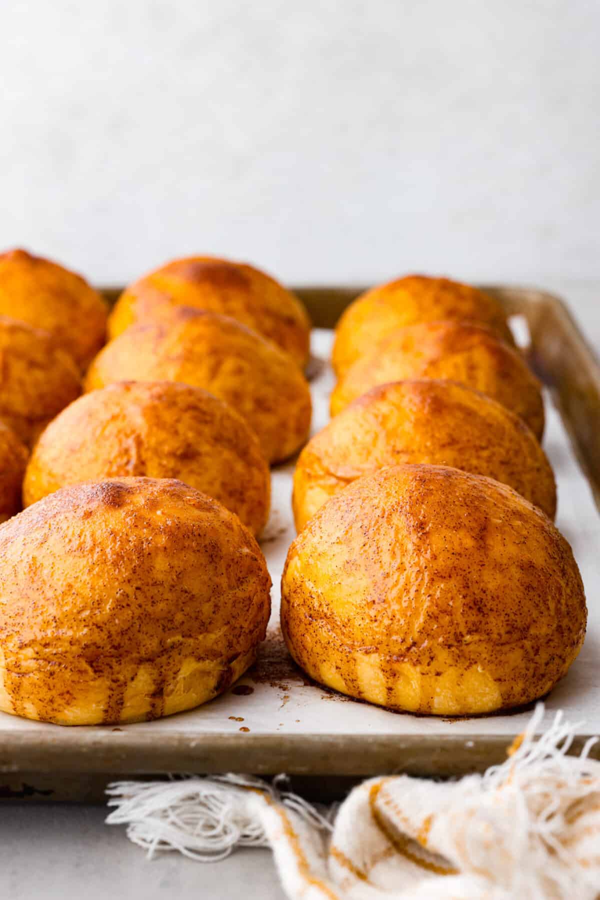 Close view of sweet potato rolls on a baking sheet pan with brown sugar glaze on top.