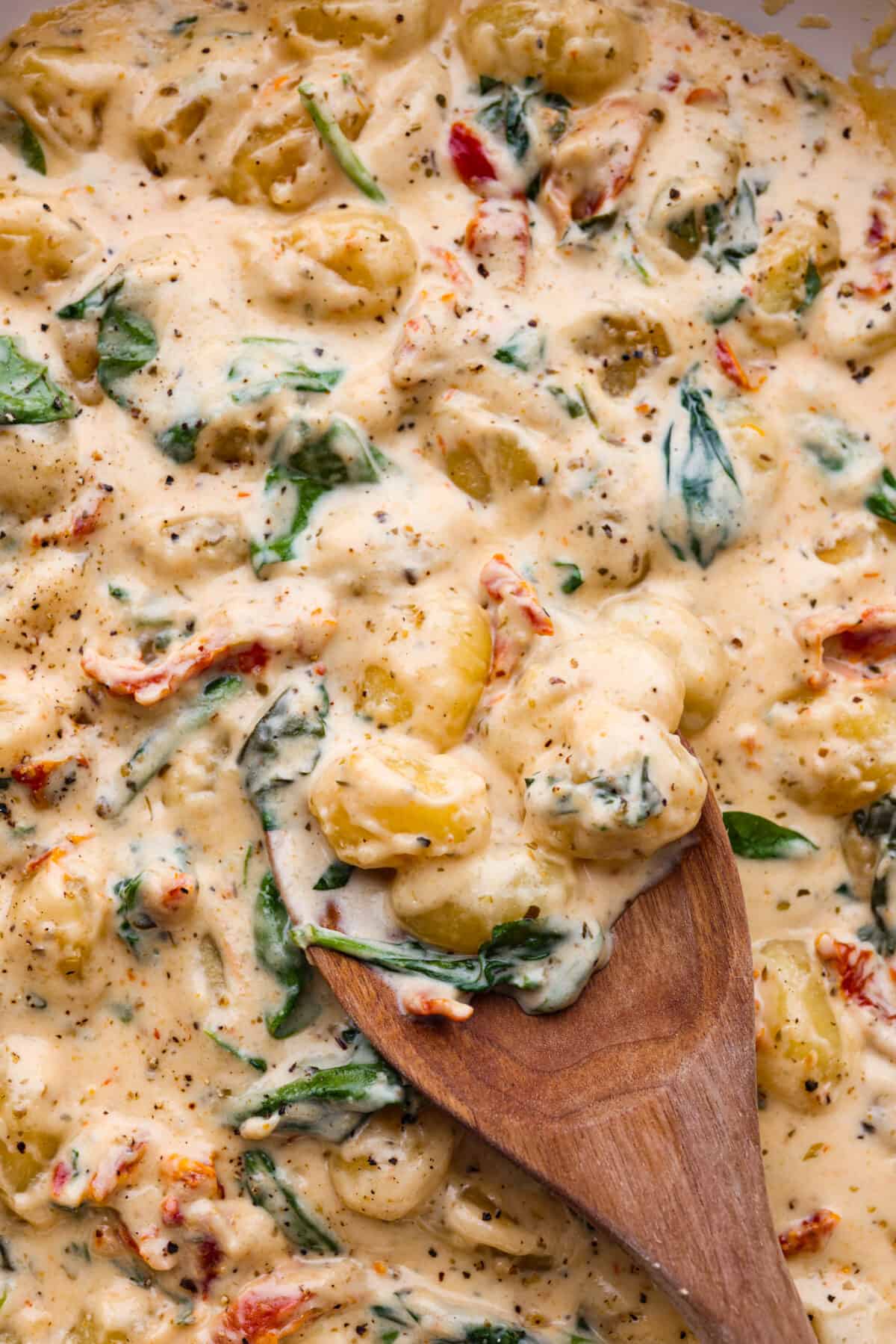 Closeup of the gnocchi in a creamy sun-dried tomato sauce. It is being stirred with a wooden spoon.