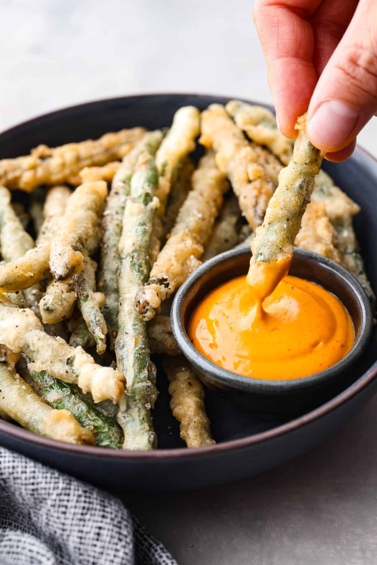 A crispy green bean being dipped into some orange sauce. 