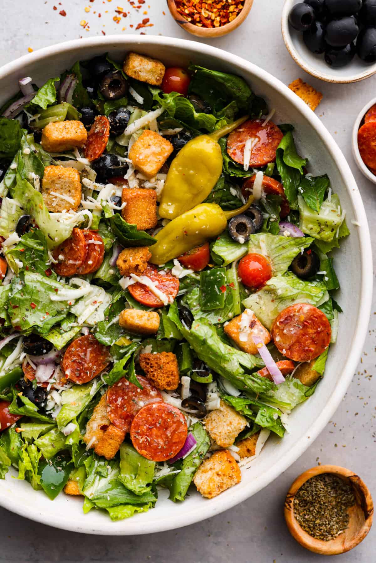 A bowl of lettuce with croutons, pepperoni, olives, tomatoes, purple onions,green bell peppers and cheese with Italian dressing. 