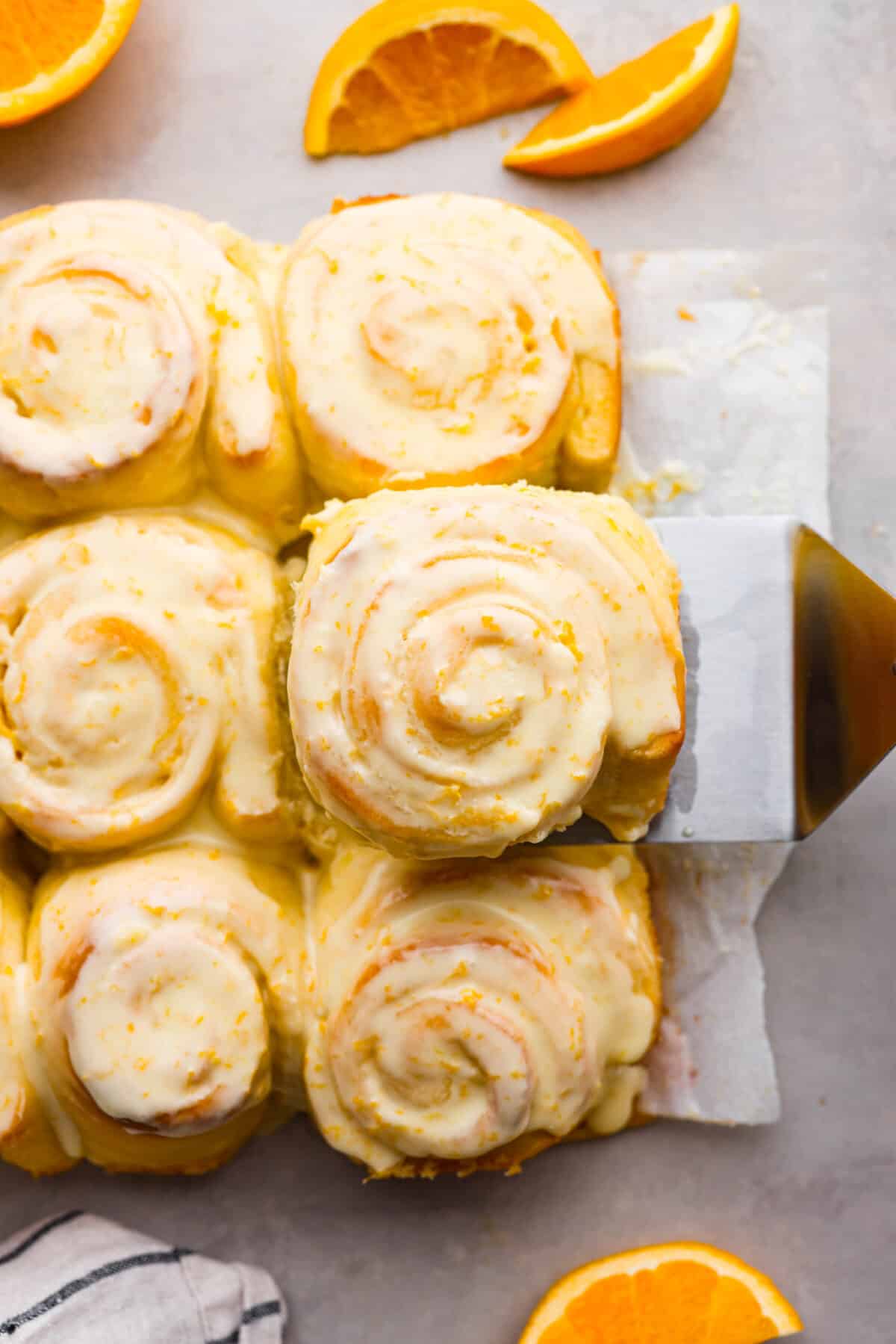 The top view of orange rolls on parchment paper surrounded by orange slices. 