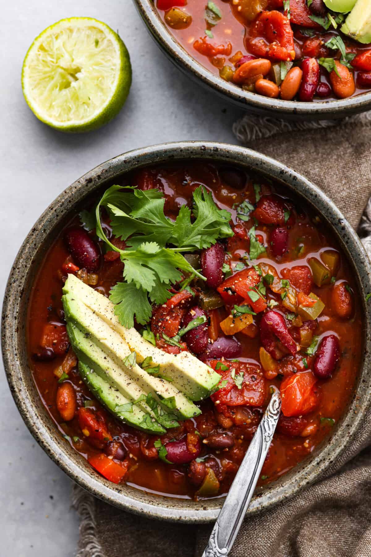 Overhead view of chili in a bowl with a spoon. Avocado and cilantro are garnished on top.