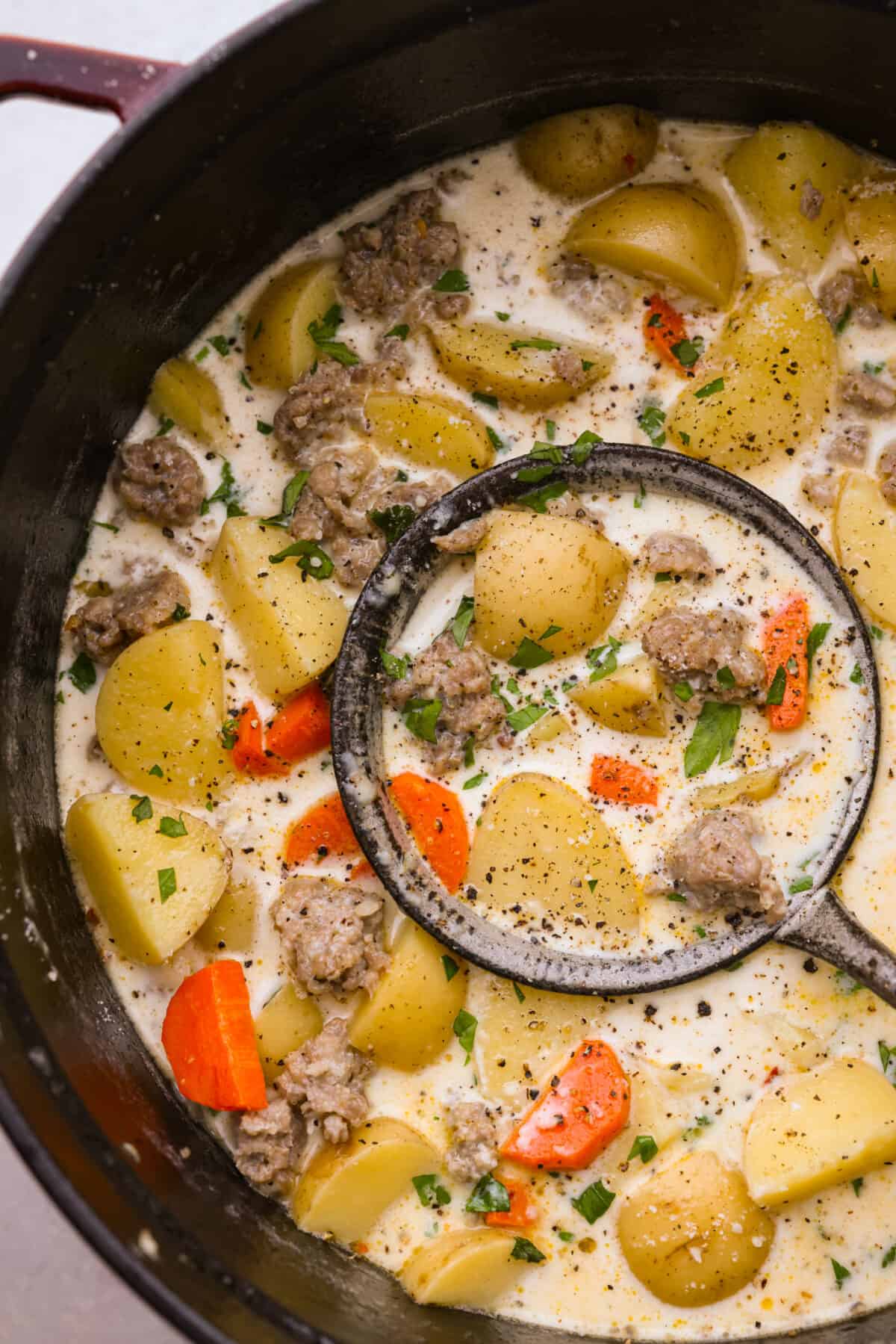 Creamy sausage and potato soup in a large pot, being scooped up with a ladle.