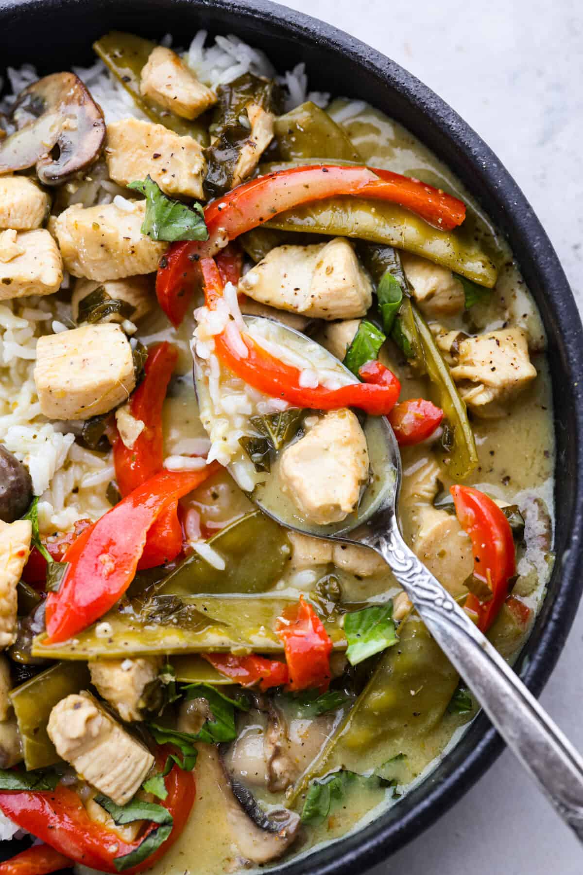 A spoonful of chicken, vegetables, and rice on a metal spoon.