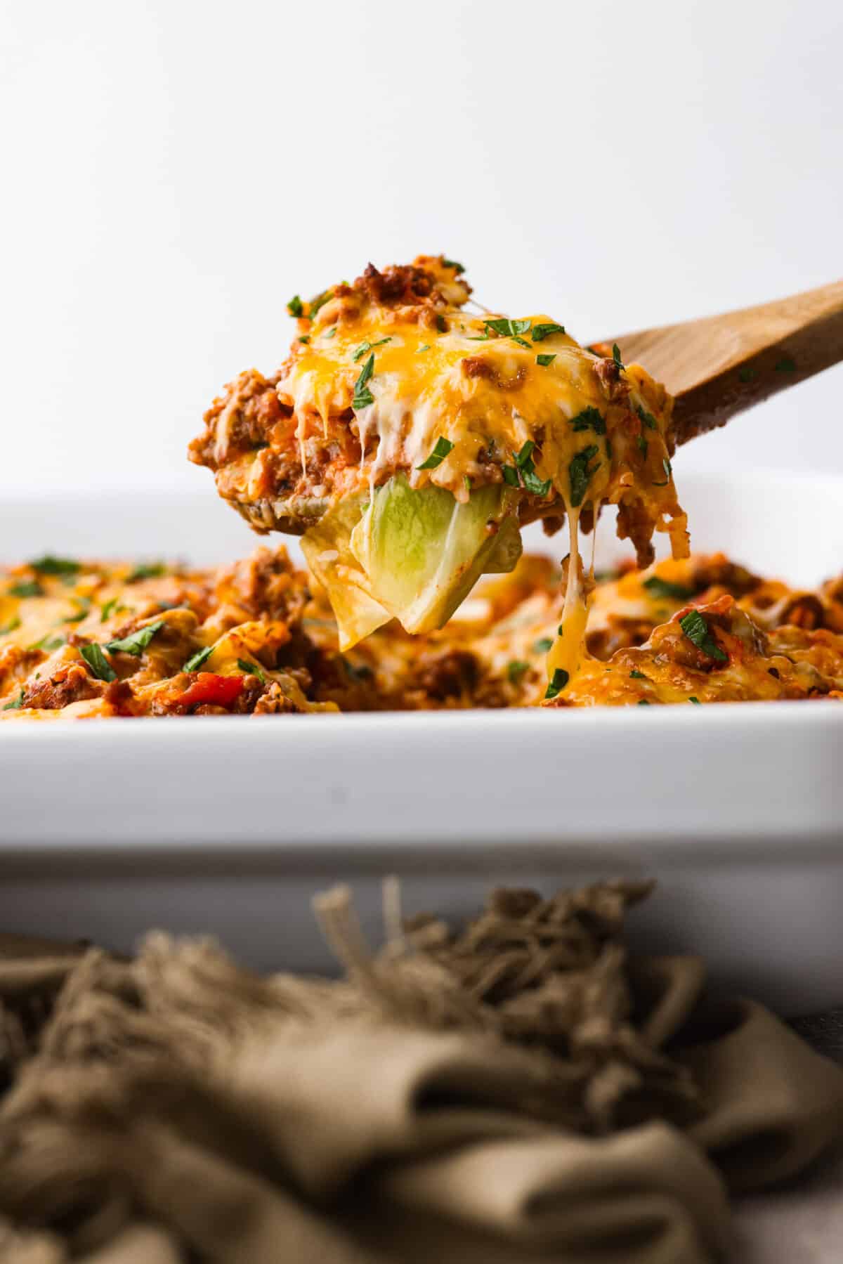 Close side view of a wood spoon lifting up a serving of cabbage roll casserole.