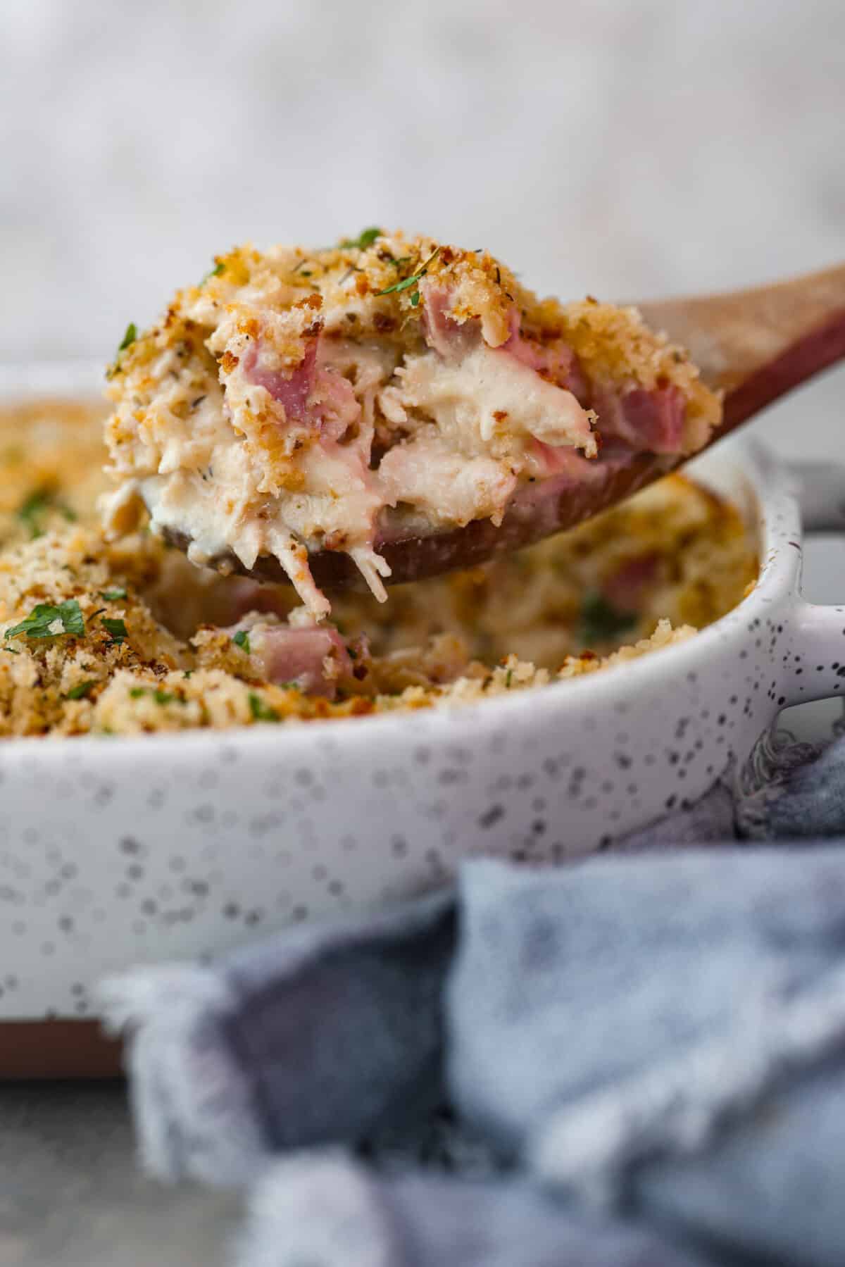 A scoop of chicken cordon bleu casserole on a wooden serving spoon.