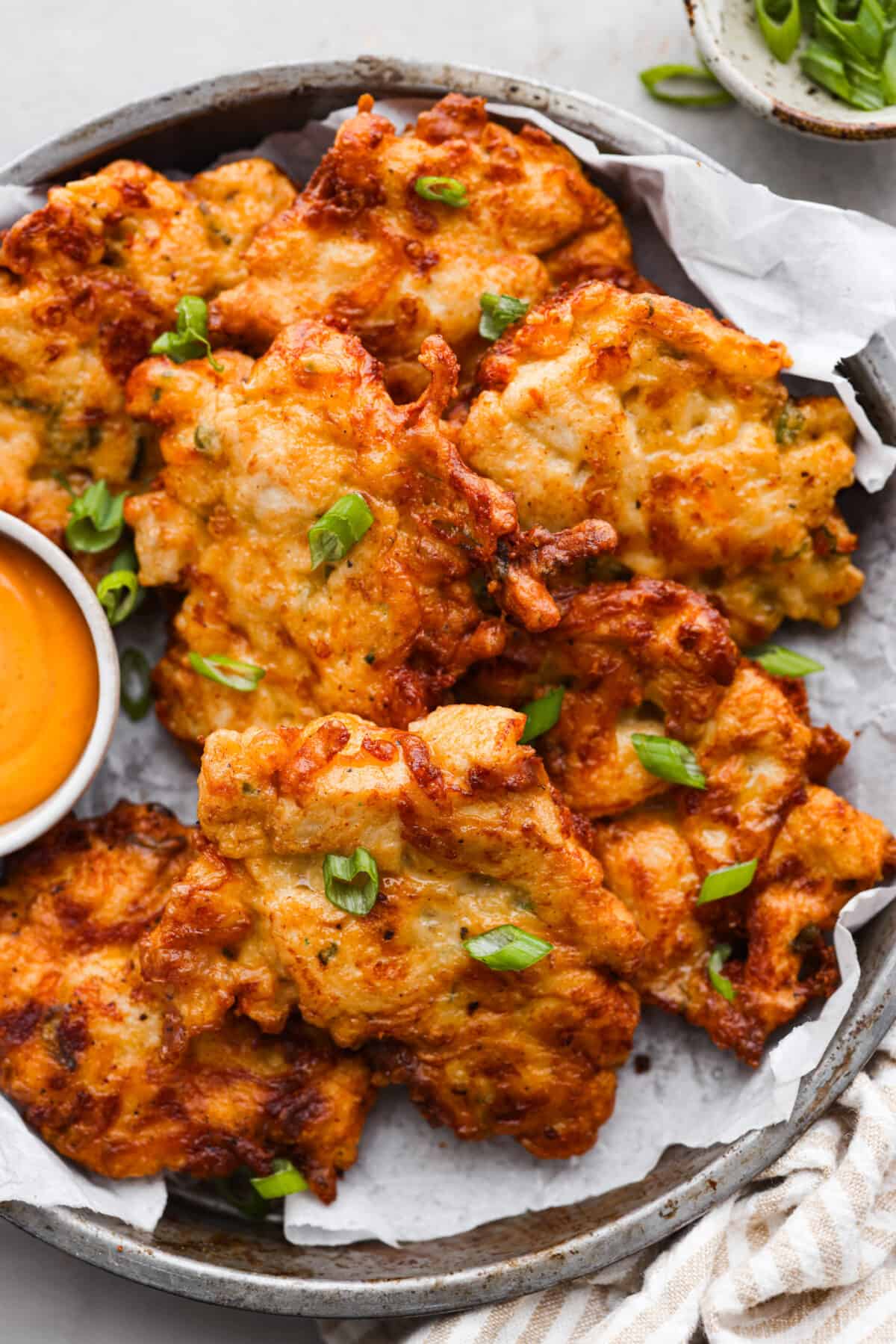 Chicken fritters in a serving dish, topped with green onions.