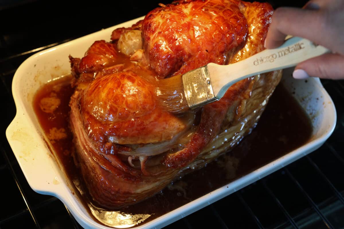 A honey baked ham with more glaze being added to it.