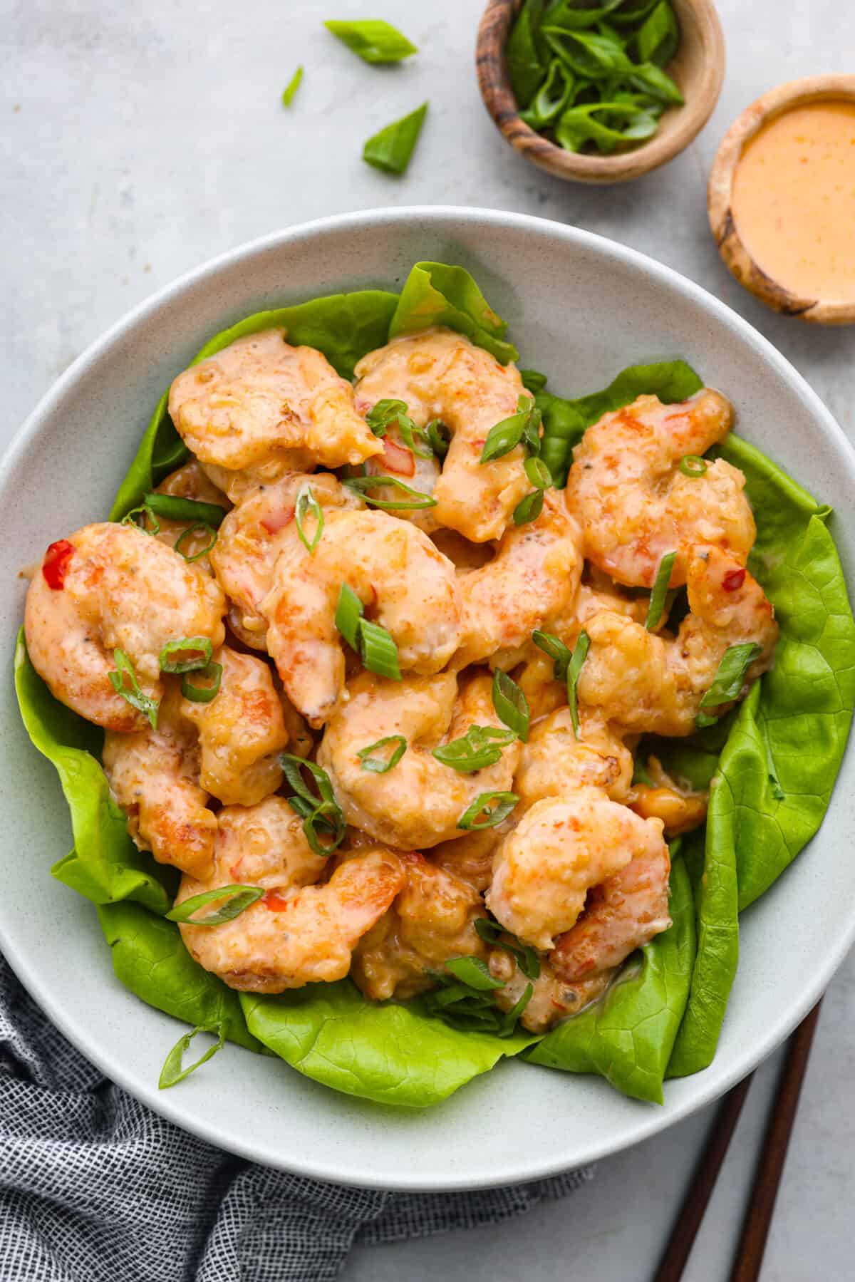 Bang bang shrimp served over a bed of greens in a white bowl.