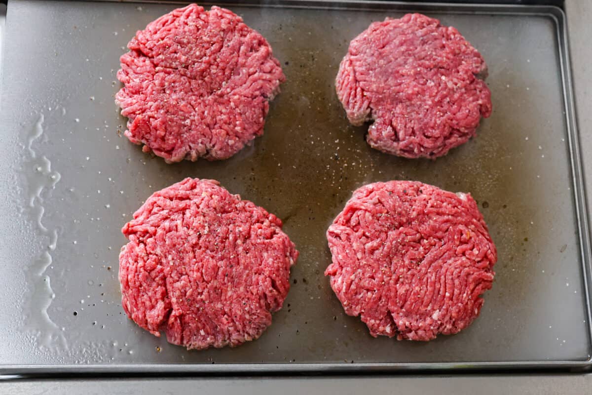 Overhead view of 4 raw beef patties on cookie sheet. 