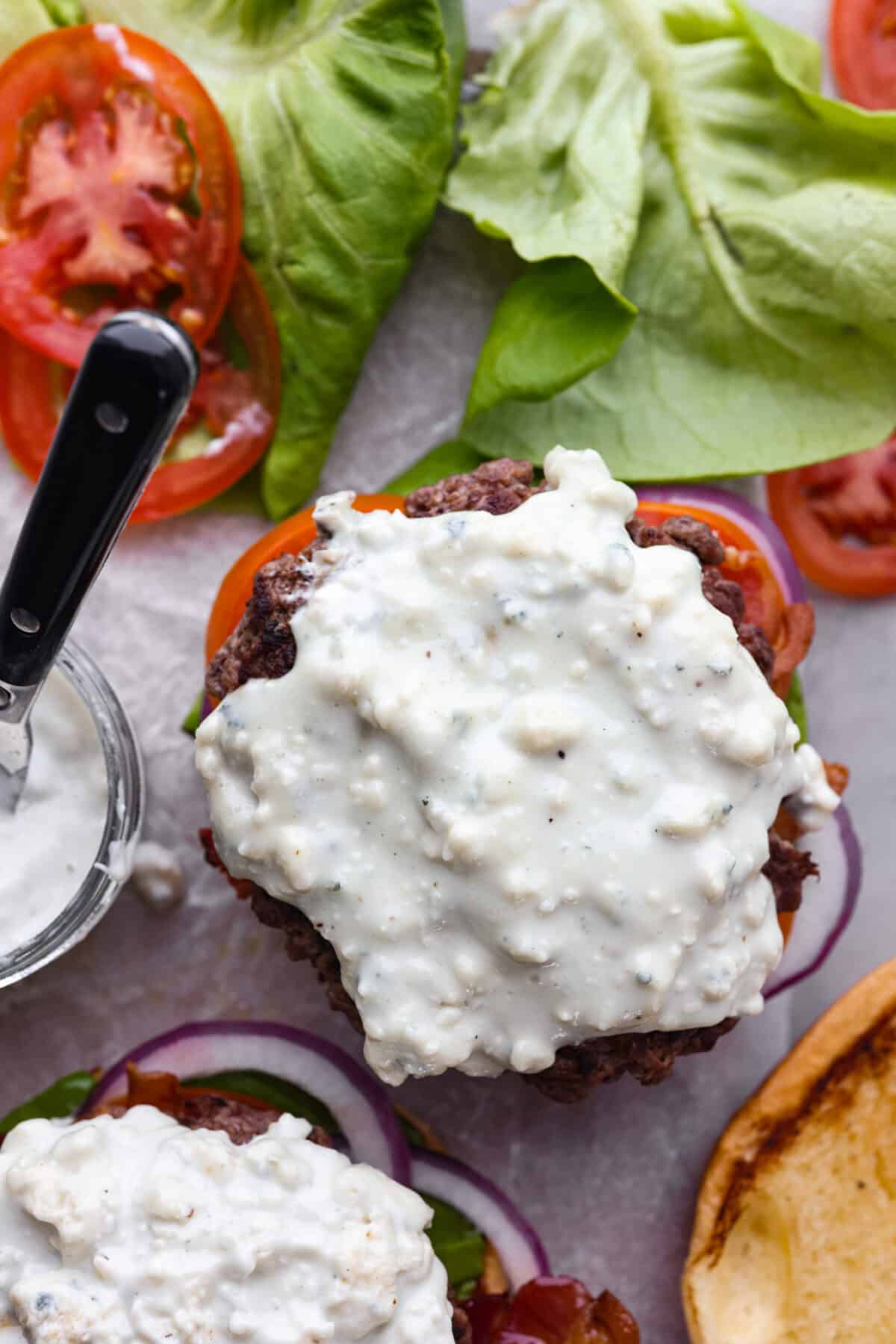 Overhead shot of burgers without top bun loaded with blue cheese dressing.