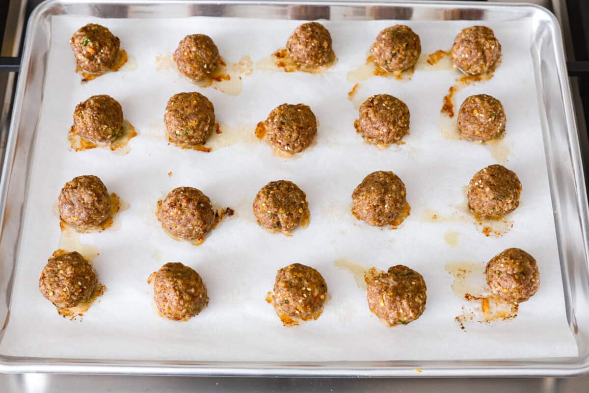 Overhead shot of parchment lined pan with rows of uncooked meatballs. 