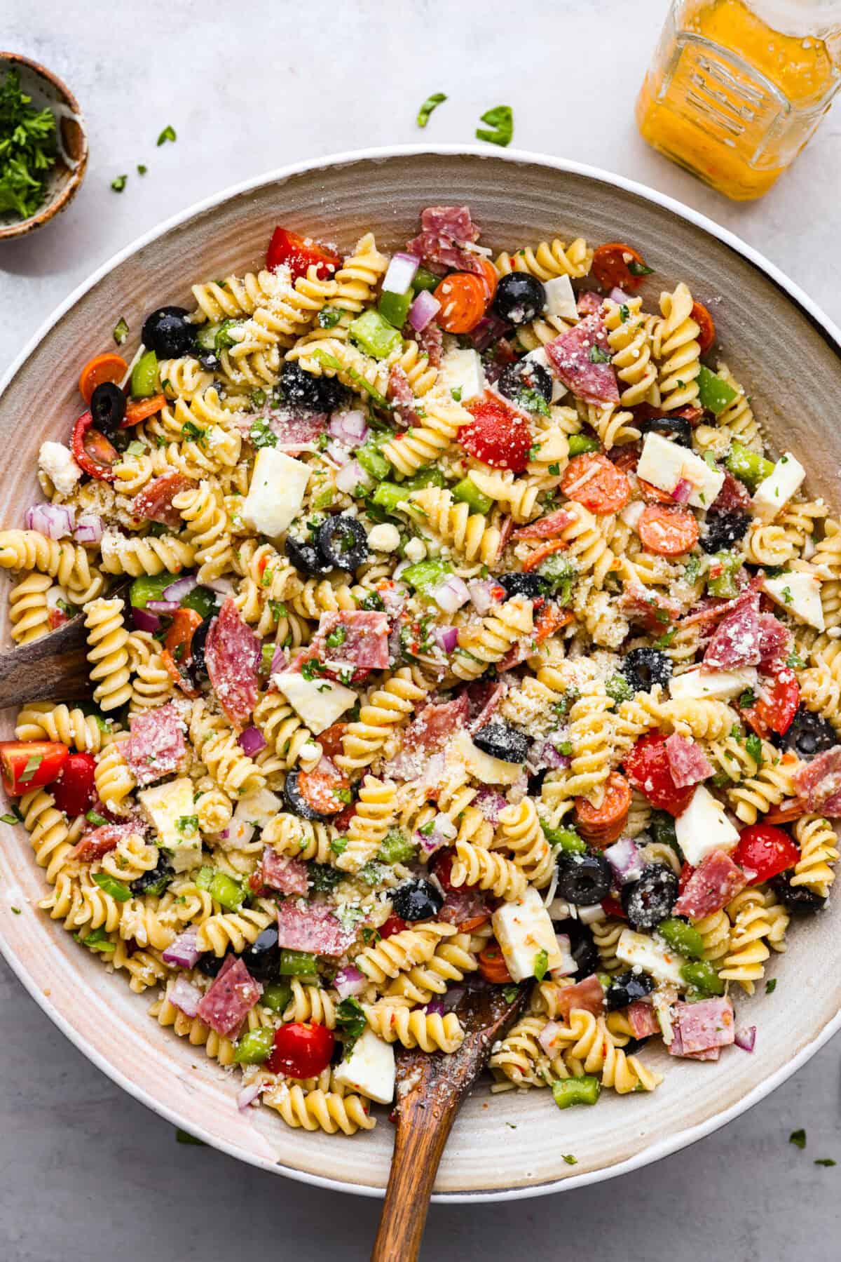 Overhead shot of a large bowl of Italian pasta salad with wooden spoon sticking out