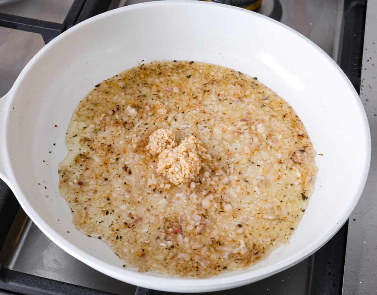 Angle shot of garlic and shallots in sauce on pan. 