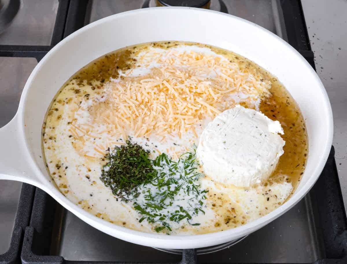 Angle shot of cheese, herbs, and cream in sauce in pan. 