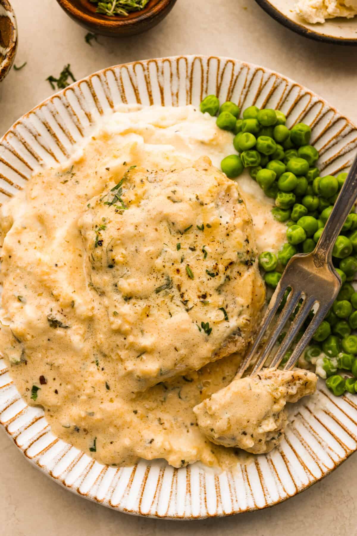 Overhead shot of plated Boursin pork chop with peas on the side and a bite skewered on a fork. 