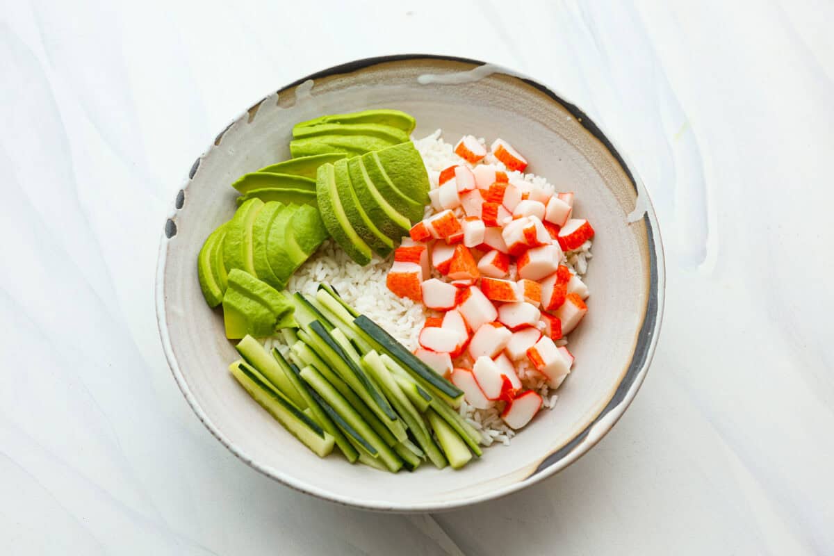 Overhead shot of bowl with rice, crab, avocado and cucumber. 